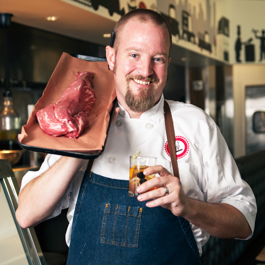 Chef Ben Phillpot with a delicious cocktail, displaying some of the all-natural, organic meat featured on the menu of Block & Grinder.