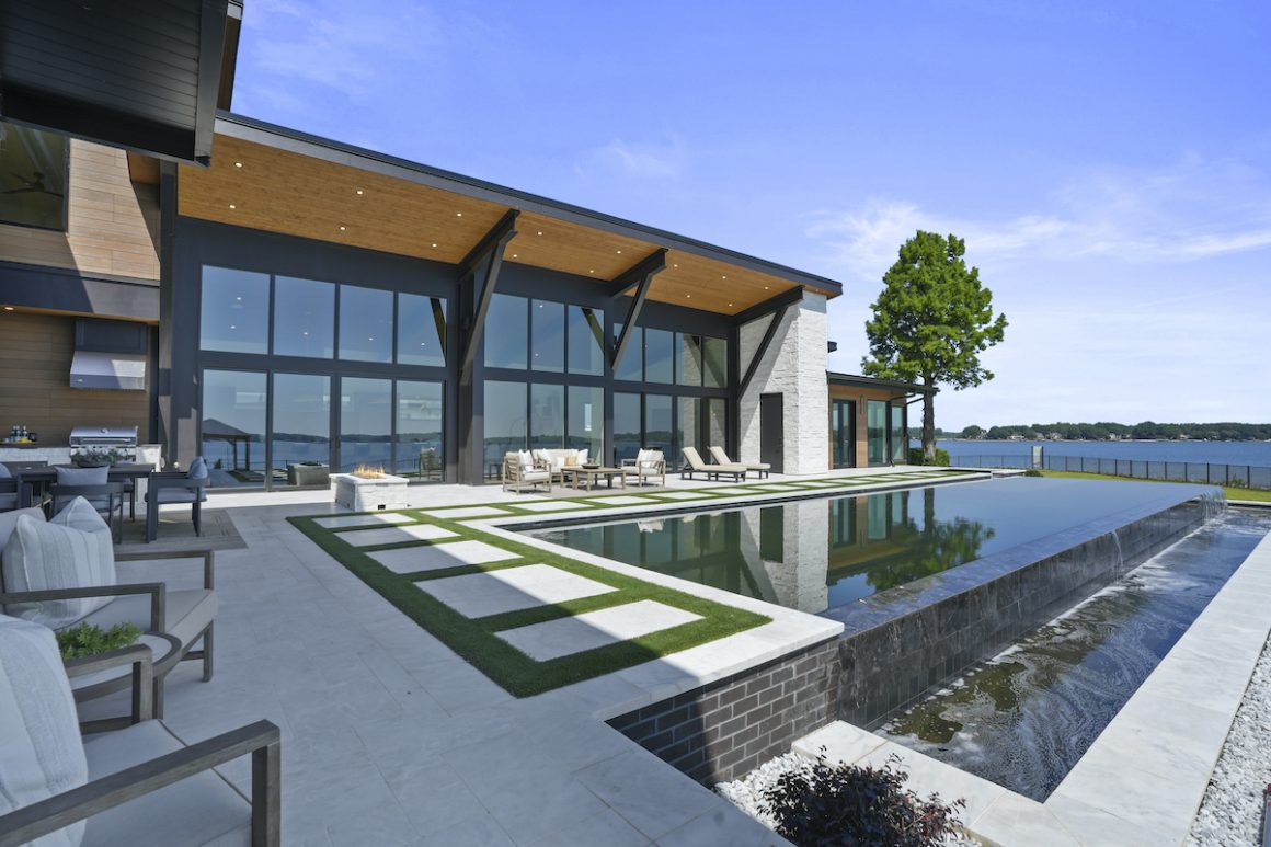 infinity pool next to a lake behind a house by grand living homes
